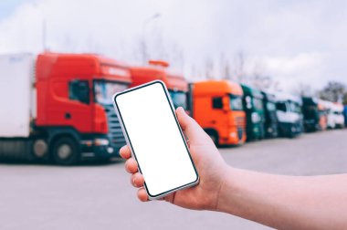 Bir adamın elinde akıllı bir telefon taklidi yap. Kırmızı kamyonların arka planına karşı. Lojistik kavramı