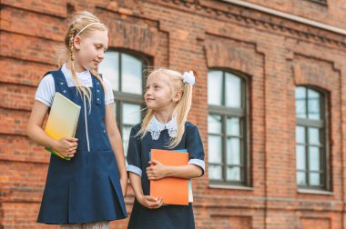 Okul üniformalı ve ellerinde kitaplarla genç kızların portresi. Eski üniversitenin arka planına karşı. Okul konseptine dönelim.