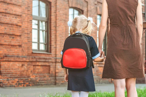 小学生和家长是紧密相连的 一个女人和一个背着背包的小女孩开始上课的时候秋天的第一天 — 图库照片