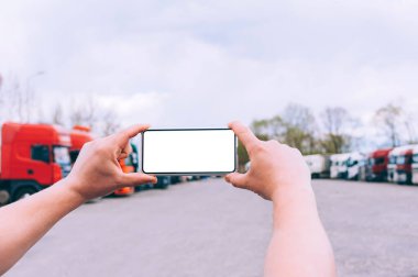 Bir adamın elinde akıllı bir telefon taklidi yap. Kırmızı kamyonların arka planına karşı. Lojistik kavramı
