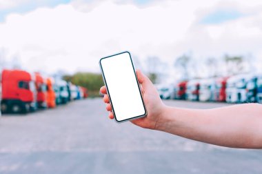 Bir adamın elinde akıllı bir telefon taklidi yap. Kırmızı kamyonların arka planına karşı. Lojistik kavramı