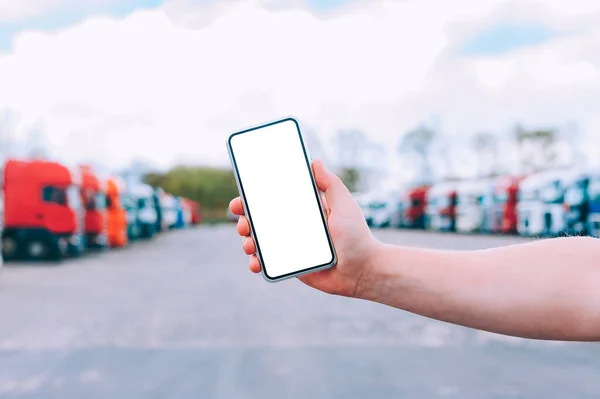 Bir adamın elinde akıllı bir telefon taklidi yap. Kırmızı kamyonların arka planına karşı. Lojistik kavramı