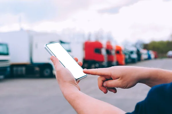 Bir adamın elinde akıllı bir telefon taklidi yap. Kırmızı kamyonların arka planına karşı. Lojistik kavramı