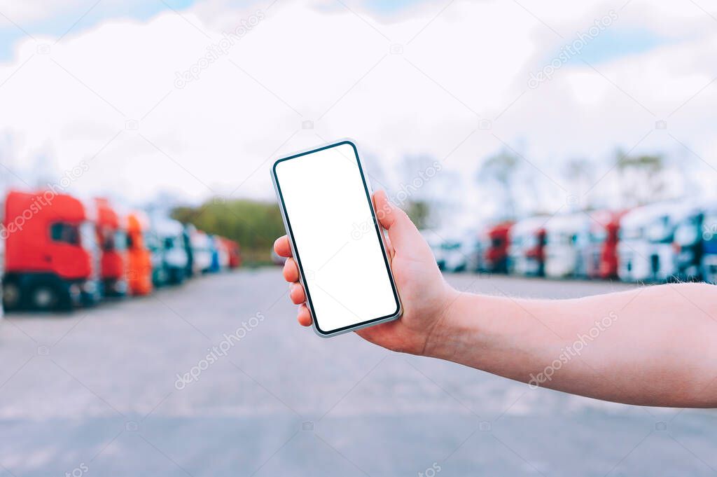 Mock up a smartphone in the hand of a man. Against the background of red trucks. Logistics concept