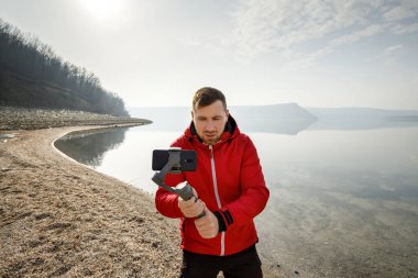 Genç bir adam telefonda elektronik dengeleyiciyle video çekiyor.