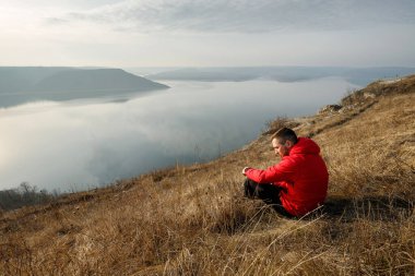 Nehrin kenarında çimenlerde oturan düşünceli bir adamın portresi.