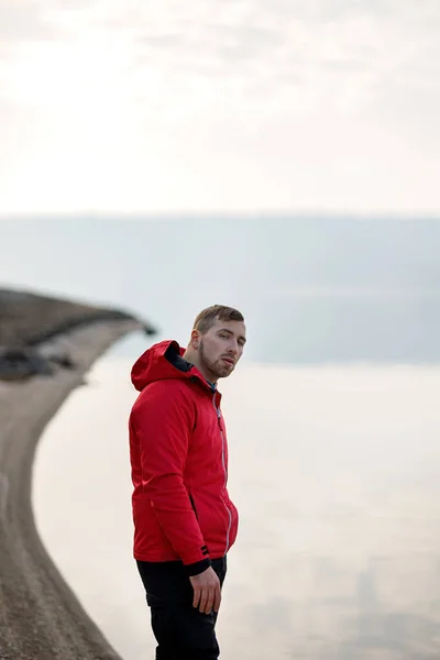 A young man in a sports suit stands by the river