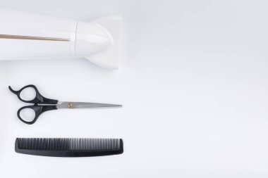 Saç makaslarını kurutmak için saç kurutma makinesi ve beyaz arka planda tarak. Üst görünüm.