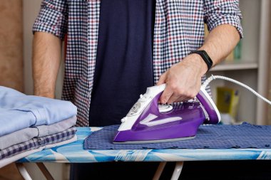 Bir adam ütü masasında ütüyle gömlek ütülüyor. Günlük ev işleri..