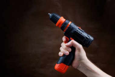 Erkek el koyu kahverengi arka planda elektrikli tornavida tutuyor..