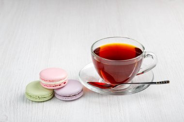 Çok renkli badem kurabiyeleri ve açık ahşap bir masada bir fincan çay. Sabah çayı ve tatlıları..