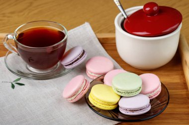 Bir fincan çay ve ahşap tepside renkli kurabiyeler. Sabah çayı ve tatlıları..