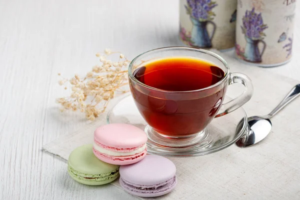 Çok renkli badem kurabiyeleri ve açık ahşap mutfak masasında bir fincan çay. Sabah çayı ve tatlıları..