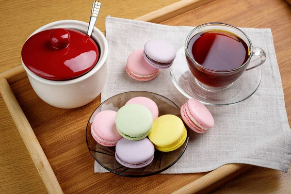 Bir fincan çay ve ahşap tepside renkli kurabiyeler. Sabah çayı ve tatlıları.