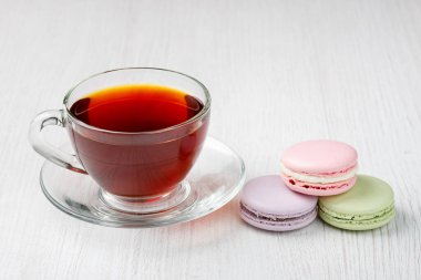 Çok renkli badem kurabiyeleri ve açık ahşap bir masada bir fincan çay. Sabah çayı ve tatlıları..