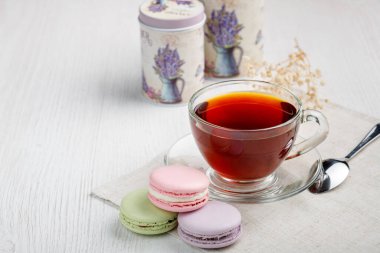 Çok renkli badem kurabiyeleri ve açık ahşap mutfak masasında bir fincan çay. Sabah çayı ve tatlıları..