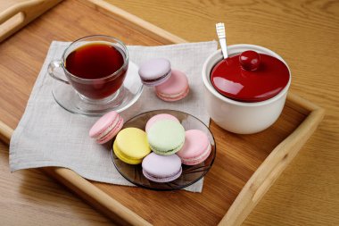 Çok renkli badem kurabiyeleri ve ahşap tepside bir fincan çay. Sabah çayı ve tatlıları..