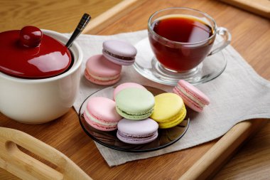 Çok renkli badem kurabiyeleri ve ahşap tepside bir fincan çay. Sabah çayı ve tatlıları..