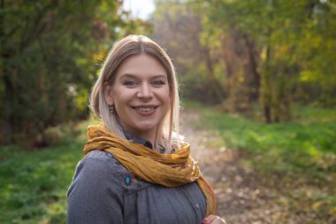 Bir sonbahar sahnesinde kameraya gülümseyen beyaz bir kadının portresi.