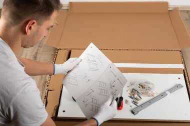 Genç adam evde yeni mobilya montajı yapıyor.