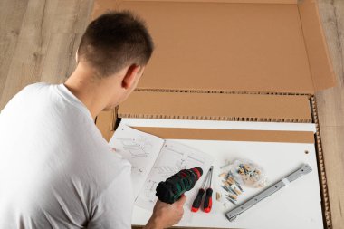 Genç adam evde yeni mobilya montajı yapıyor.