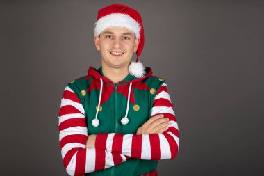 Grinch kostümü giyen yakışıklı adamın portresi gri arka planda kameraya gülümsüyor.