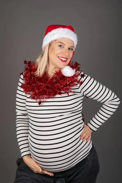 三个月前 漂亮的孕妇头戴圣诞帽 头戴灰色背景的红色圣诞花环 — 图库照片