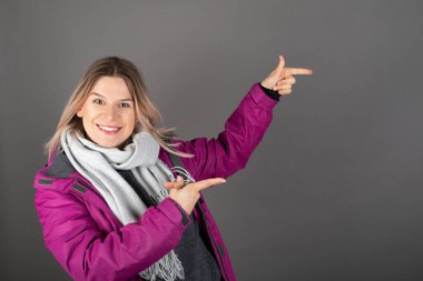 Kış elbisesi giymiş güzel genç bir kadının gri sırt grubundaki bir şeyi göstermesi.