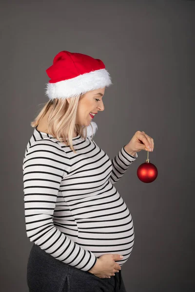 第三季的孕妇穿着圣诞饰物 摆出灰色背景的姿势 — 图库照片