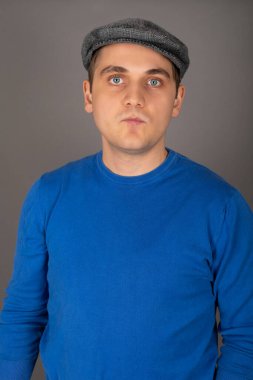 Gri arkaplan önünde kameraya bakan mavi gözlü yakışıklı sarışın bir adamın portresi.