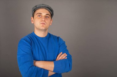 Mavi gözlü yakışıklı bir sarışın ressamın portresi, kollarını gri arkaplanda kavuşturan etkileyici bir görünüm.