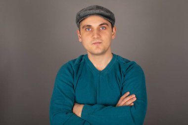 Mavi gözlü yakışıklı bir sarışın ressamın portresi, kollarını gri arkaplanda kavuşturan etkileyici bir görünüm.