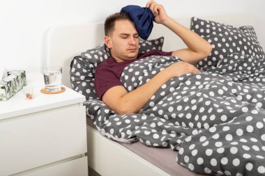 Covid-19 'u olan genç bir erkek hasta yatakta yatıyor, ciddi bir baş ağrısı var.