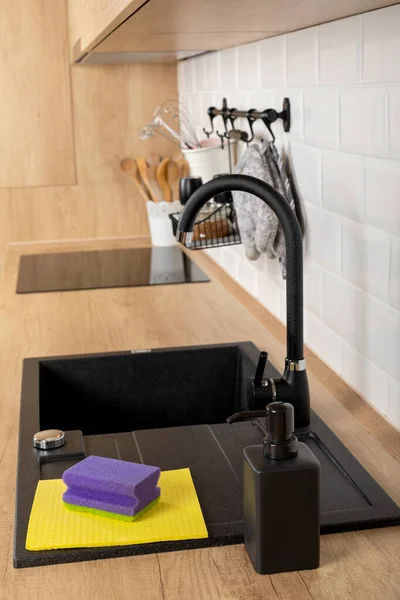 一个干净的木制厨房台面和带有清洁用品的黑色水槽的近照 — 图库照片