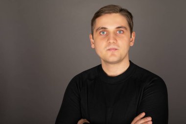 Siyah bluz giyen, gri arka planda poz veren beyaz yakışıklı bir adamın portresi.