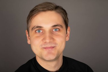 Siyah bluz giyen, gri arka planda poz veren beyaz yakışıklı bir adamın portresi.