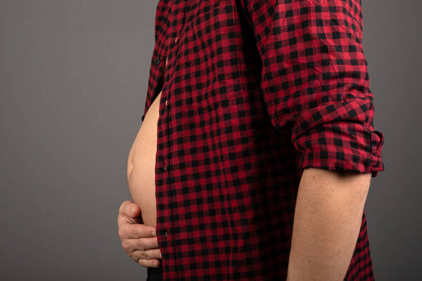 Close up picture of young man's bloated stomach in front of grey background