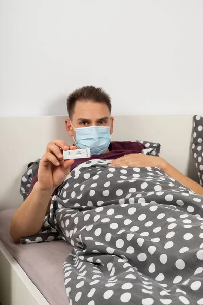 집에서 침대에 Covid Male Patient Holding Quick Antigen Covid Test — 스톡 사진