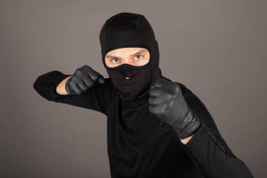 Tehlikeli bir suçlu kameraya doğru vuruyor, siyah maske ve takım elbise giyiyor.