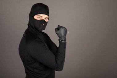 Siyah takım elbiseli ve yüzünde maske olan hırsız elleri kelepçeli poz veriyor.