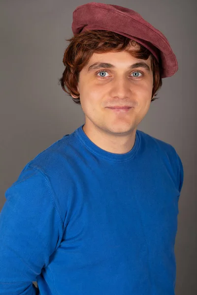 Portrait of a young handsome male actor wearing wig and hat, posing in front of grey background