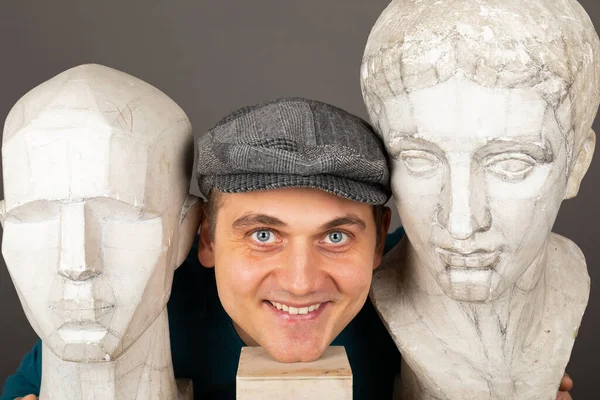 Portrait of a young creative male artist holding a gypsum statues head in front of grey background
