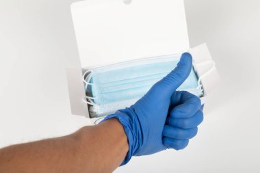 Bir kutu koruyucu maske taşıyan mavi eldivenli insan elinin resmini kapat.