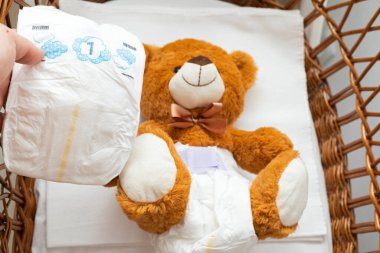 Bebek yatağında bebek bezi takmış kahverengi bir ayı heykeli.