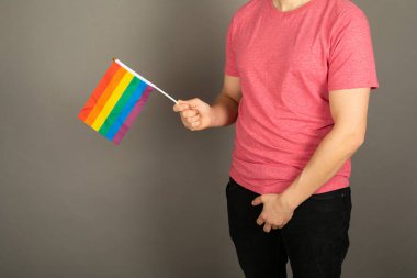 Pembe tişört ve gökkuşağı bayrağı giymiş eşcinsel bir adam.