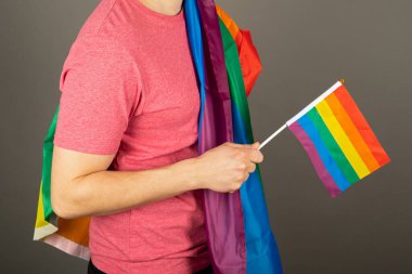 Pembe tişört ve gökkuşağı bayrağı giymiş eşcinsel bir adam.