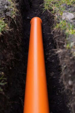 Turuncu PVC drenaj borularını yere seriyor.