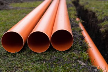 Turuncu PVC drenaj borularını yere seriyor.