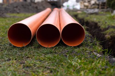 Turuncu PVC drenaj borularını yere seriyor.