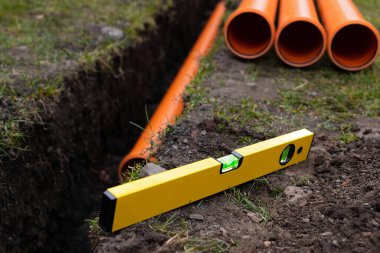 Turuncu PVC drenaj borularını yere seriyor.